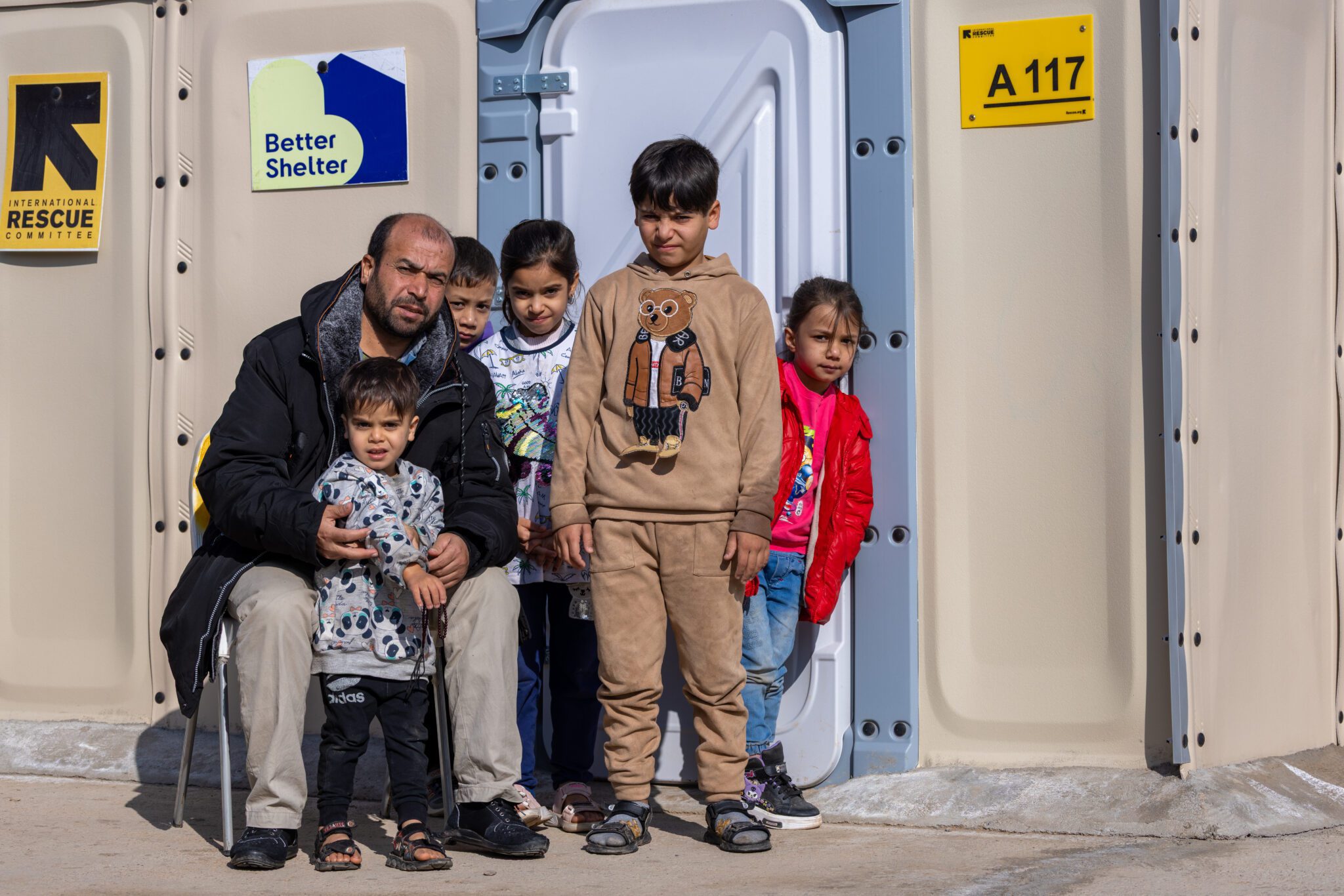 Support at the border for families returning to Afghanistan A family outside their temporary shelter at the IRC Temporary Relief Facility (TRF) in Islam Qala. The IRC provides short-term accommodation through Relocatable Housing Units (RHUs) donated by Better Shelter for families returning from Iran. © The International Rescue Committee. Abdul Khaliq Sediqi/IRC